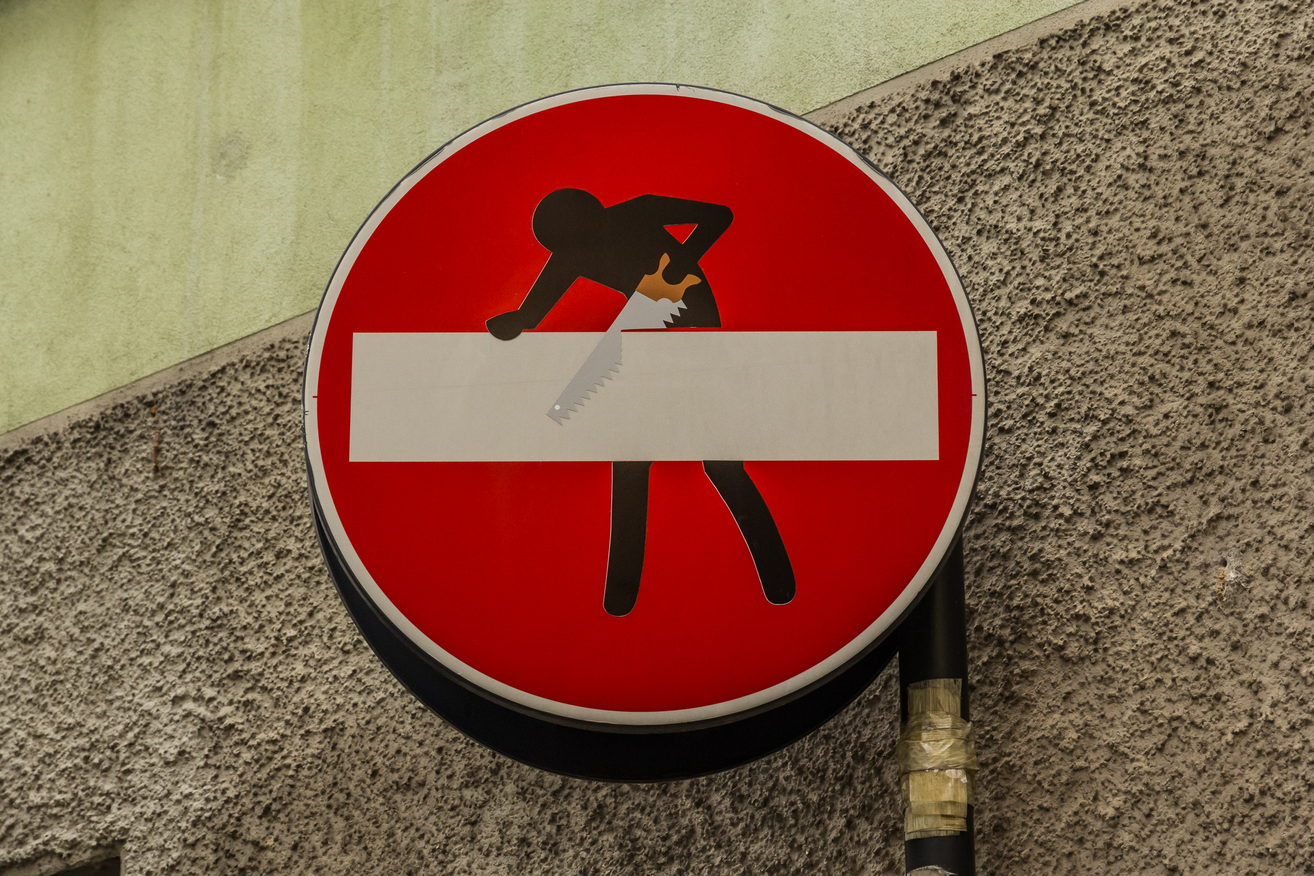 Street-Art an einem Einbahnschild – ein Männchen sägt den Balken durch