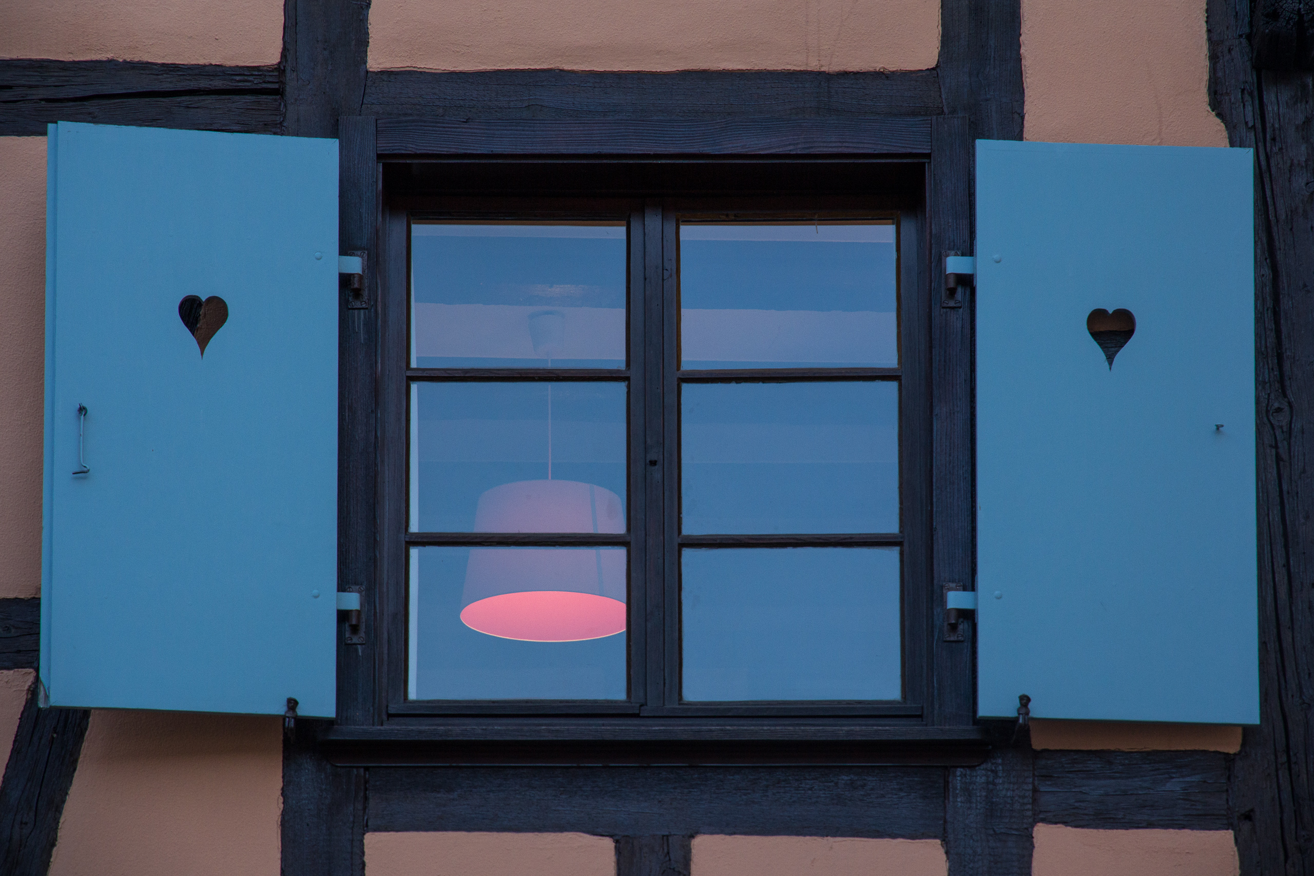 Hellblaue Fensterläden mit ausgesägtem Herz, drinnen brennt die Lampe
