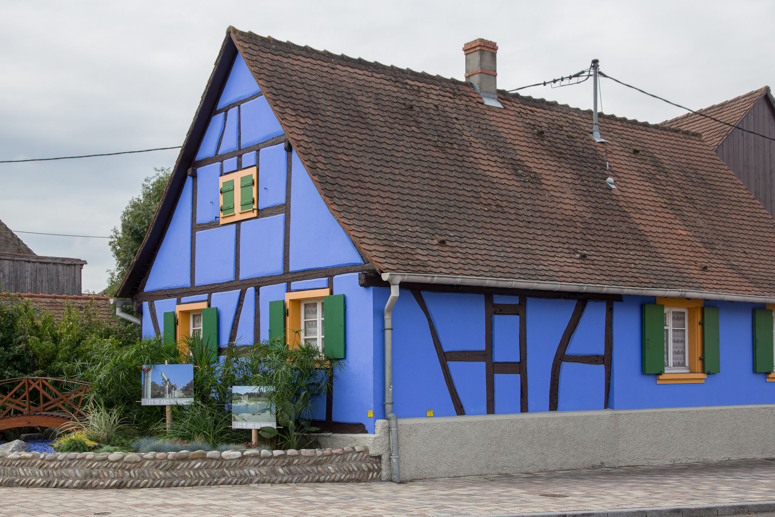 Knallblaues Fachwerkhaus, davor die Tafeln „10 Jahre Brücke“